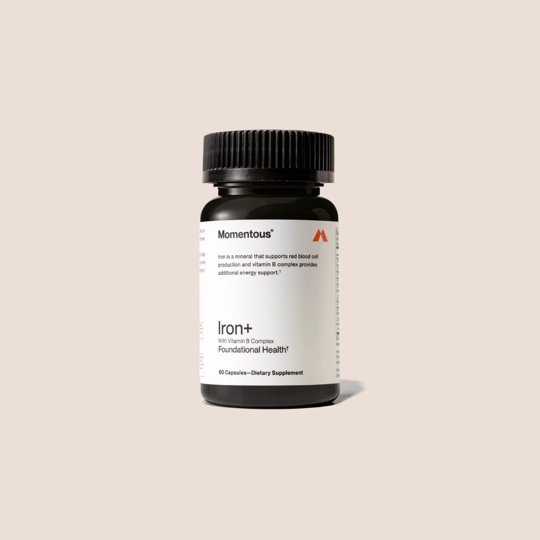 A bottle of Momentous Iron+ dietary supplement capsules with a black cap and white label is shown against a plain beige background.