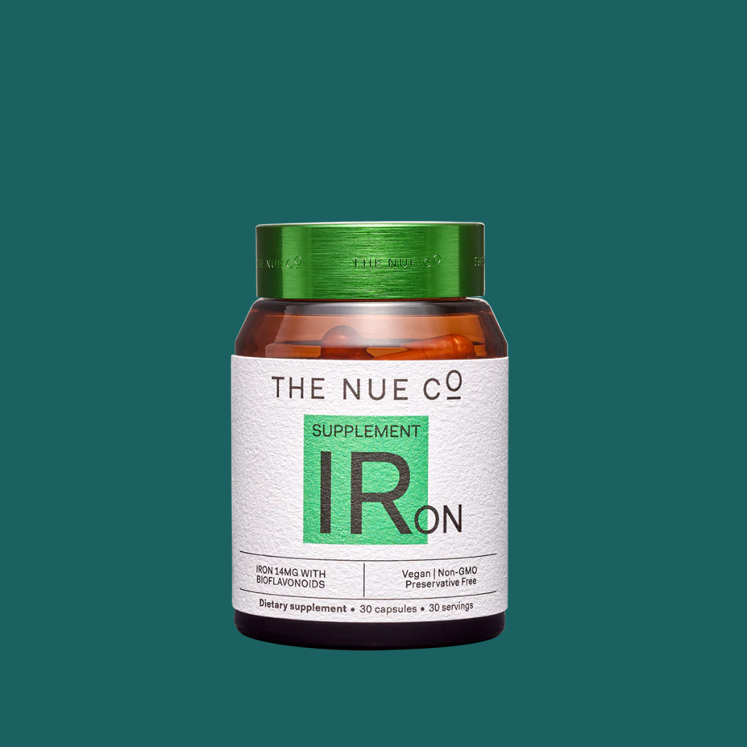 A bottle of The Nue Co. Iron supplement capsules with a white and green label against a solid teal background.