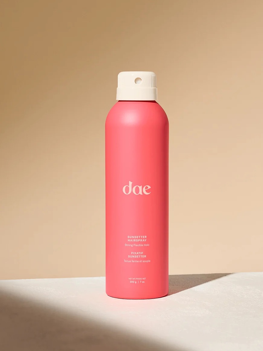 A pink spray bottle labeled "dae" stands upright on a beige surface with a neutral background.