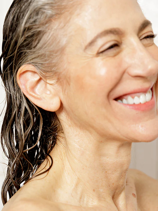 Close-up of a smiling woman with wet hair, showing her face and shoulder, with a bright and natural expression.