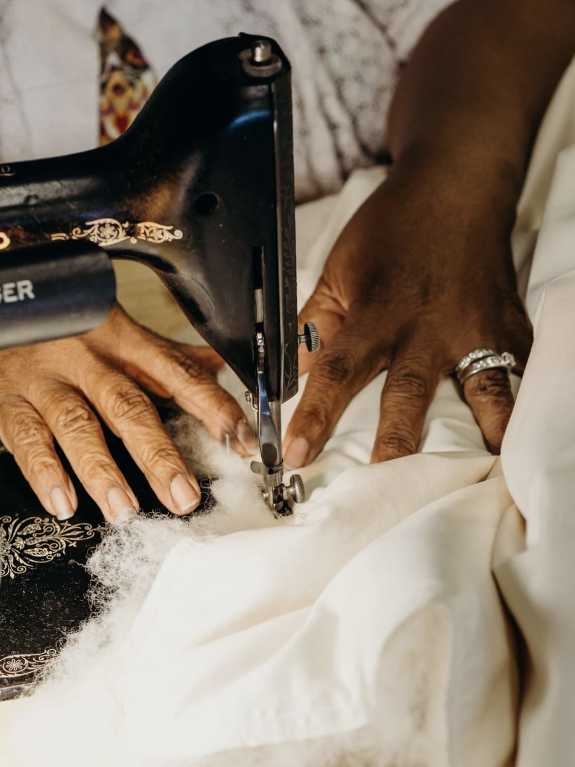 Close-up of a person’s hands guiding fabric through a vintage sewing machine, with visible stuffing material under the needle.