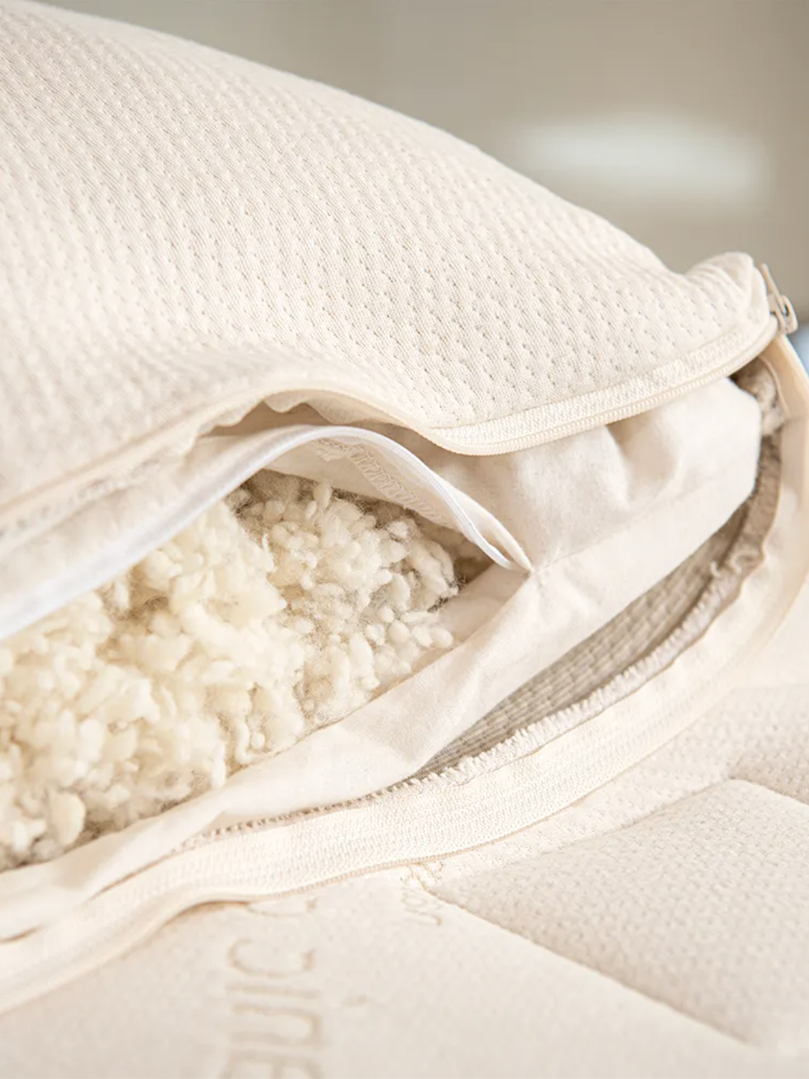 A close-up of a beige pillow with a zipper partially open, revealing shredded filling material inside.