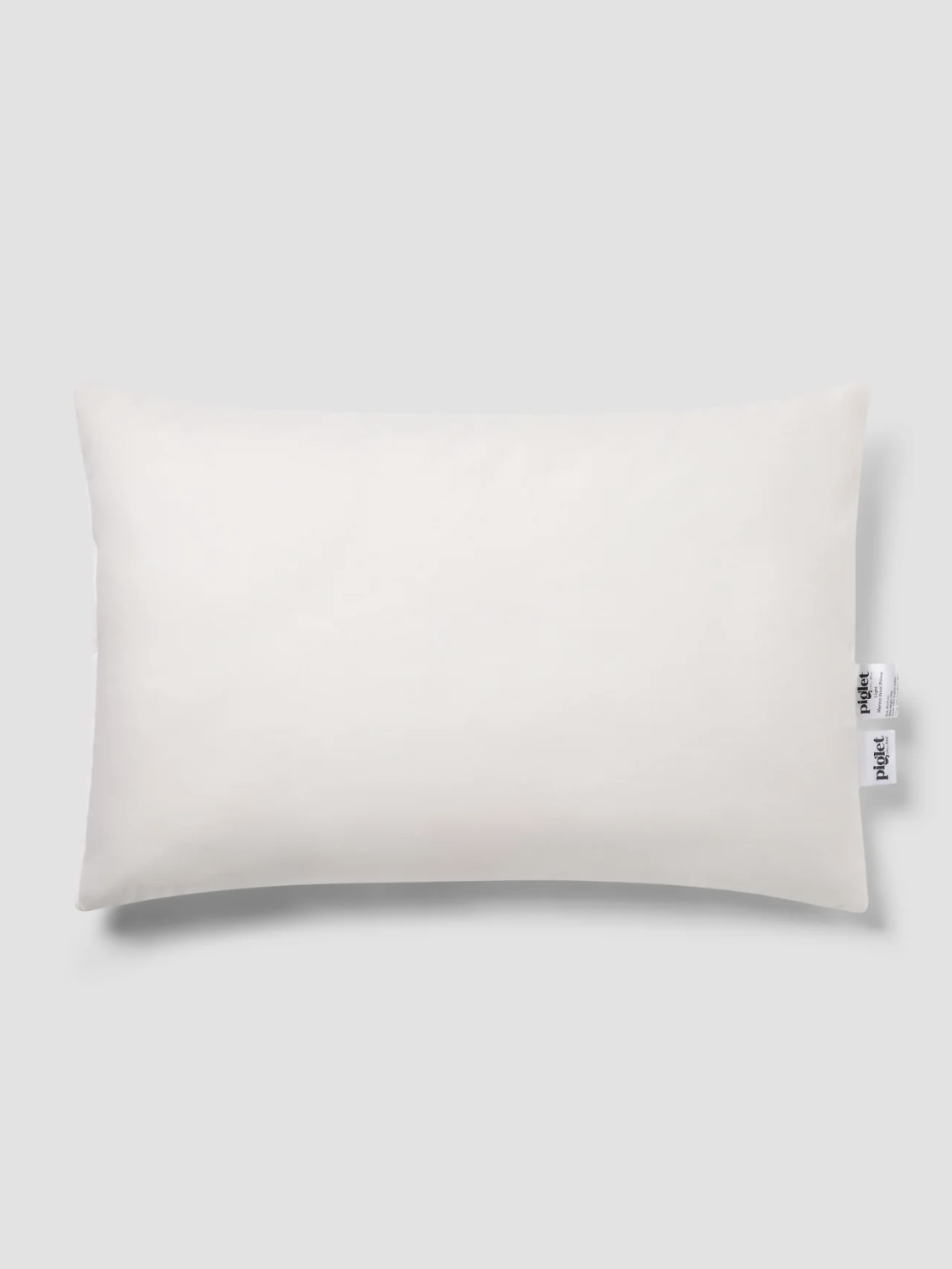 Rectangular white pillow with two tags on the right side, placed on a plain light gray background.