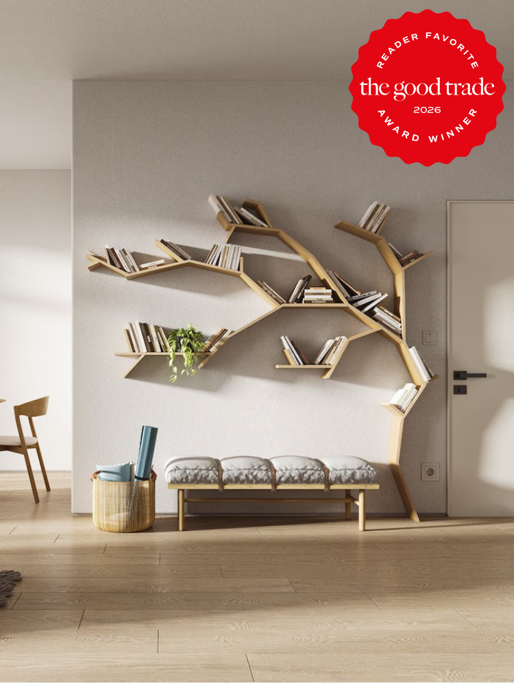 A tree-shaped wooden wall bookshelf holds books above a cushioned bench in a minimalist room; a red "The Good Trade 2026 Award Winner" badge is in the top right corner.