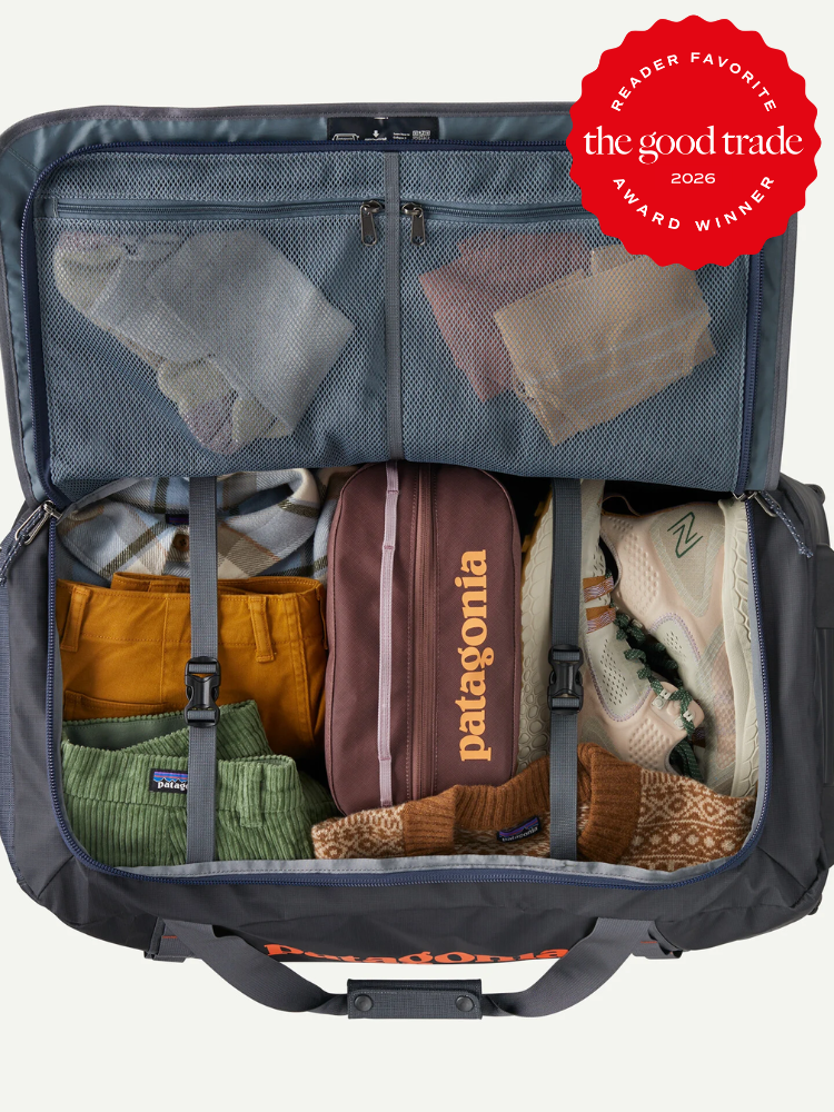 An open duffel bag neatly packed with folded clothes, shoes, and a zippered pouch. A "The Good Trade Award Winner 2026" badge is displayed in the top right corner.