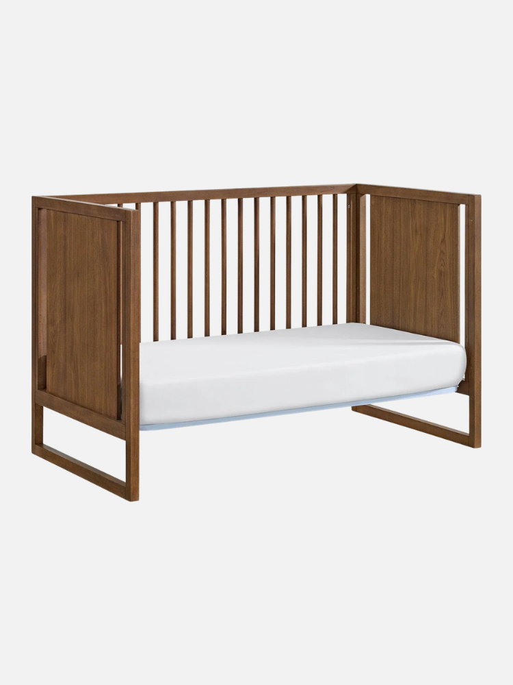 A wooden toddler bed with side rails and solid headboard and footboard, featuring a white mattress on a minimalist frame.
