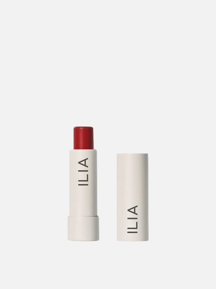 A tube of ILIA lipstick with the cap removed and placed beside it, showing a red lipstick bullet in a white cylindrical container.