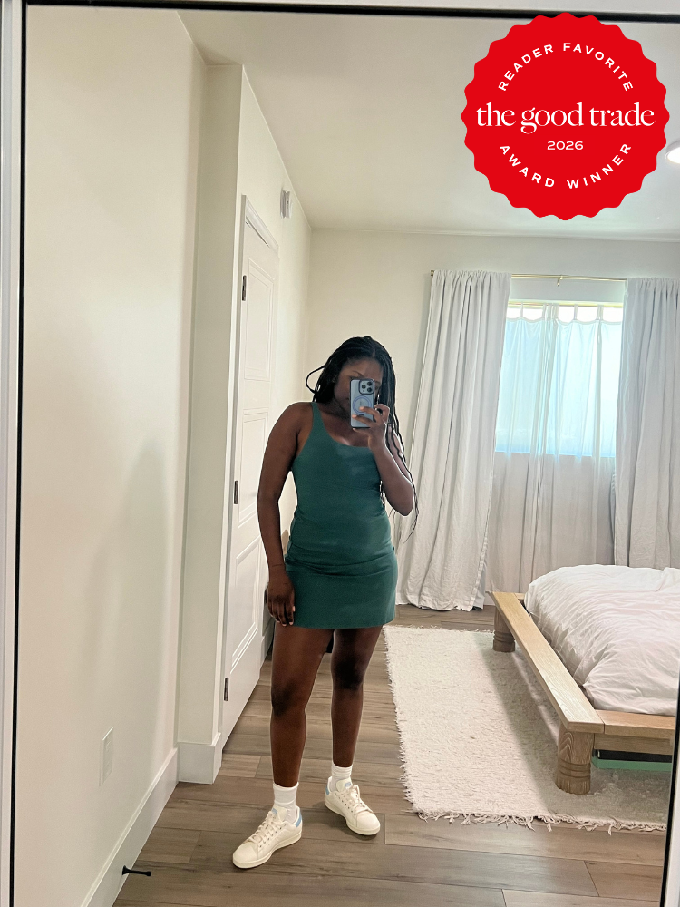A woman takes a mirror selfie in a bedroom, wearing a green sleeveless dress and white sneakers. A red "The Good Trade 2026 Award Winner" badge appears in the upper right corner.