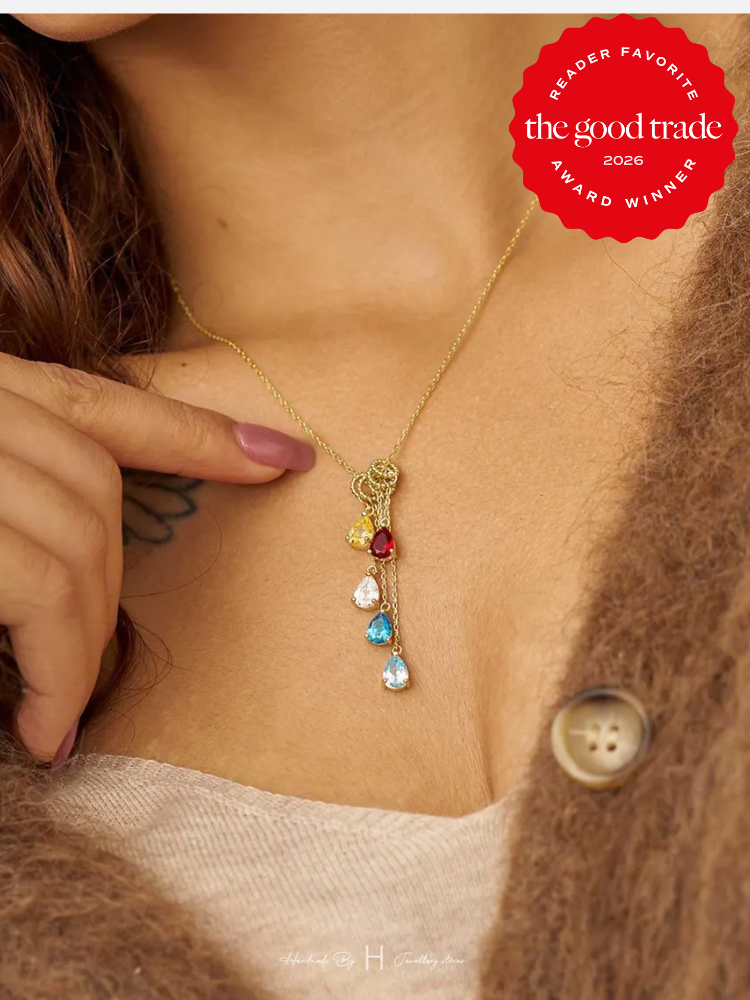 A person wearing a gold necklace with five colorful gemstone pendants, holding the chain with one hand—perfect for online shopping inspiration; a "The Good Trade 2026 Award Winner" badge appears in the corner.