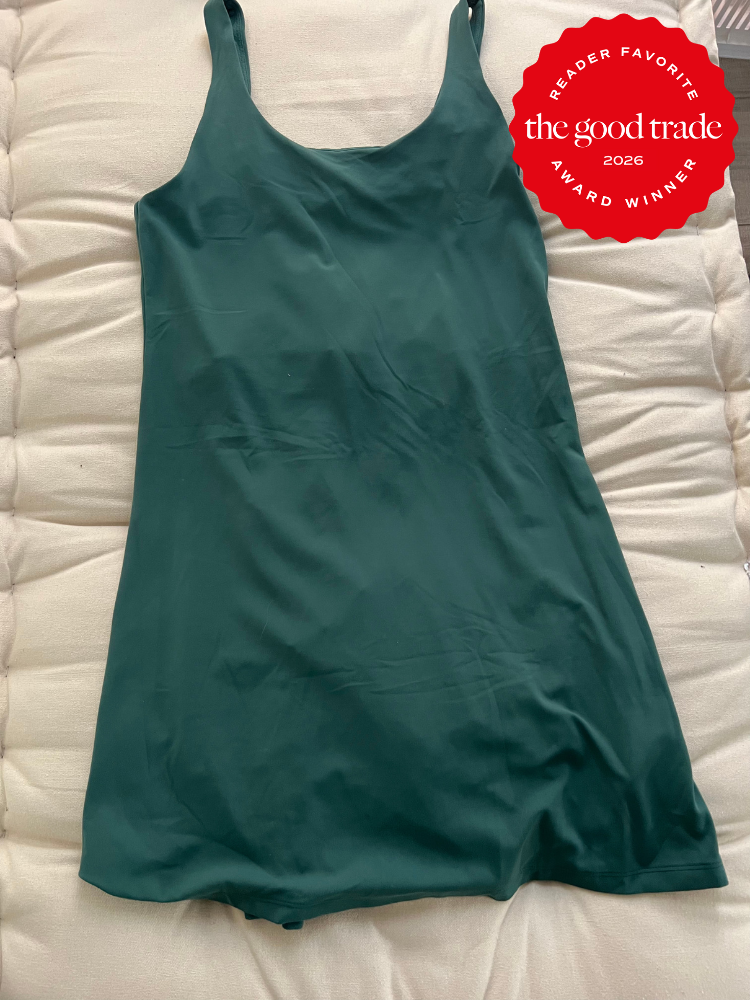 A dark green sleeveless dress is laid flat on a light-colored quilted surface. A red badge reads, "The Good Trade Reader Favorite Award Winner 2026.