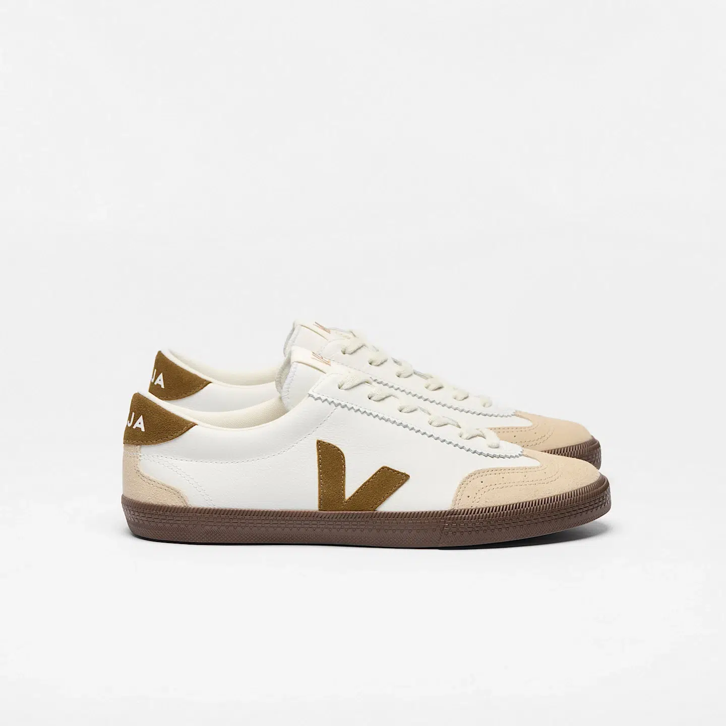 A pair of low-top sneakers with white leather uppers, beige suede accents, brown rubber soles, and a brown "V" logo on the sides—perfect for adding a touch of French girl fashion to your everyday look.