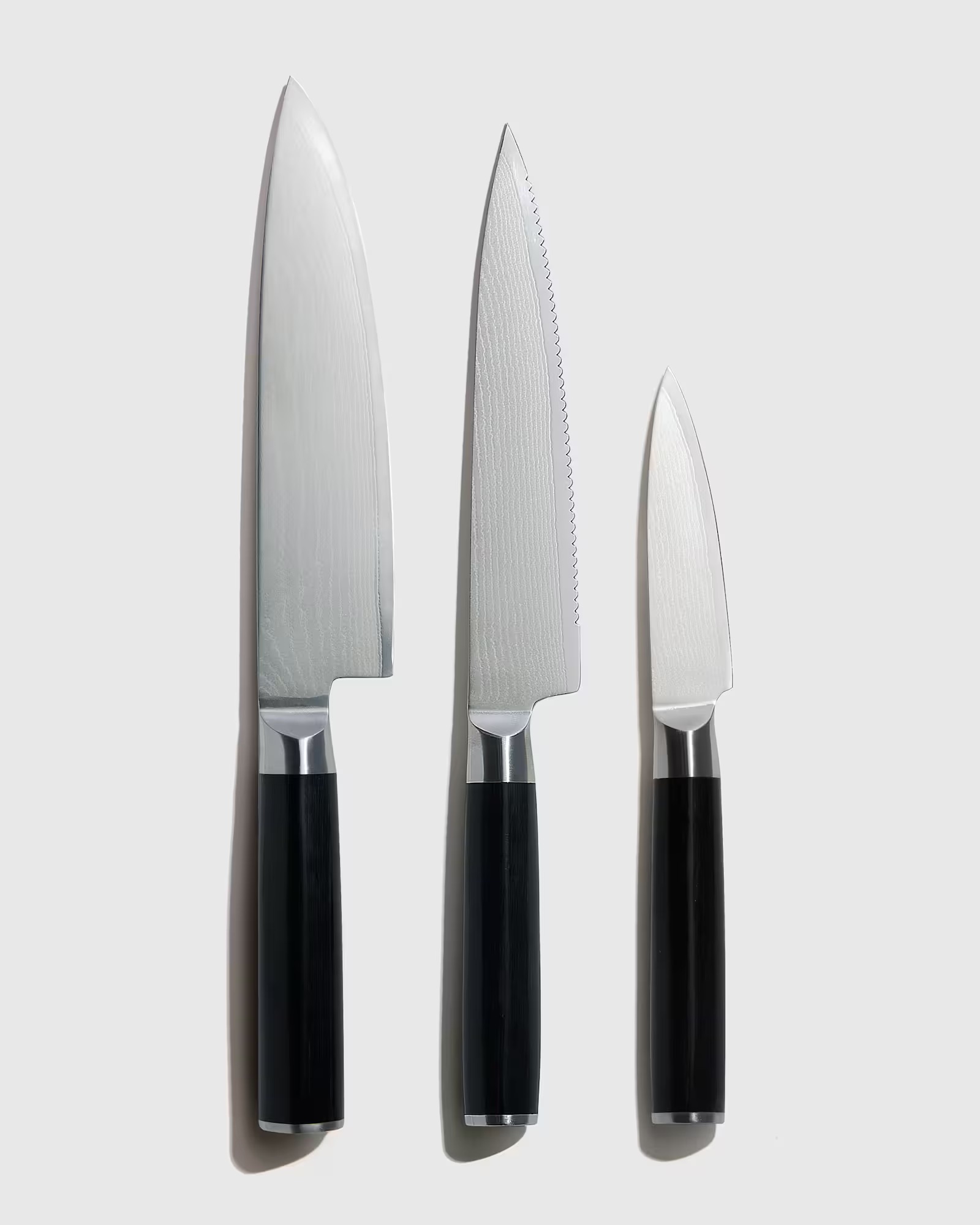 Three kitchen knives with black handles and silver blades are arranged vertically side by side on a plain light background.