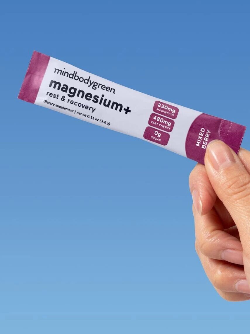A hand holds a single-serve packet of mindbodygreen magnesium+ rest & recovery supplement against a blue background, labeled as "bestseller.
