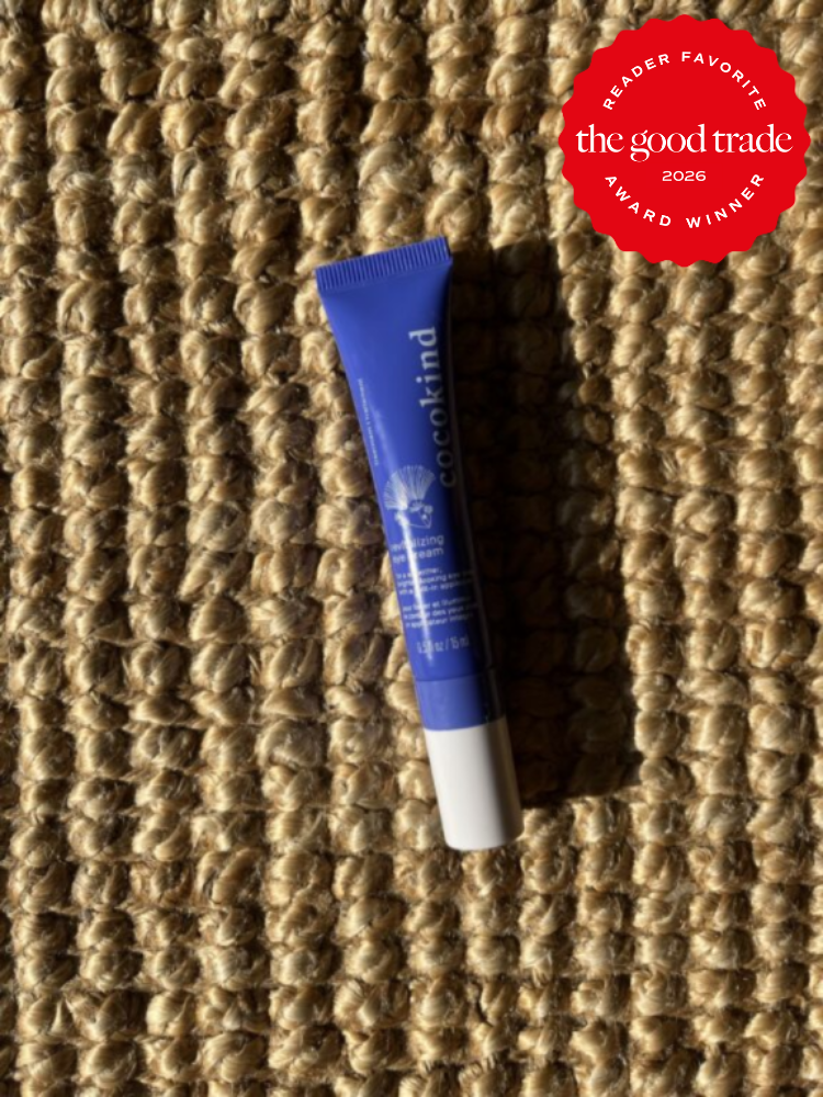 A blue tube of Cocokind eye cream lies on a woven straw surface. A red badge in the corner reads "The Good Trade 2026 Reader Favorite Award Winner.