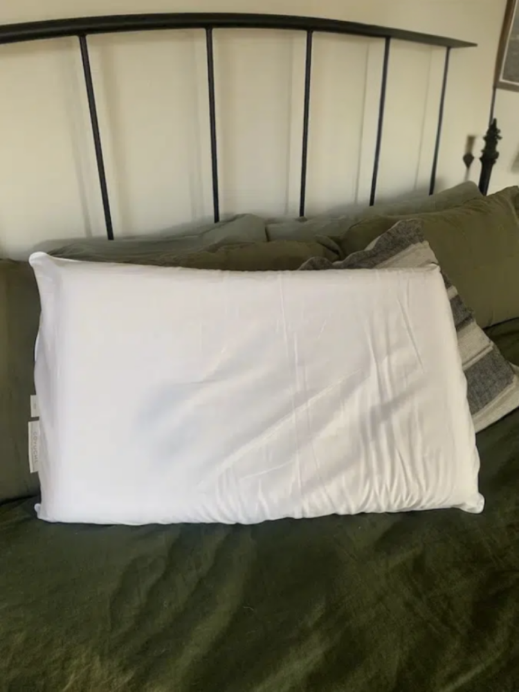 A white pillow with a slightly wrinkled cover rests against green bedding and a black metal headboard.