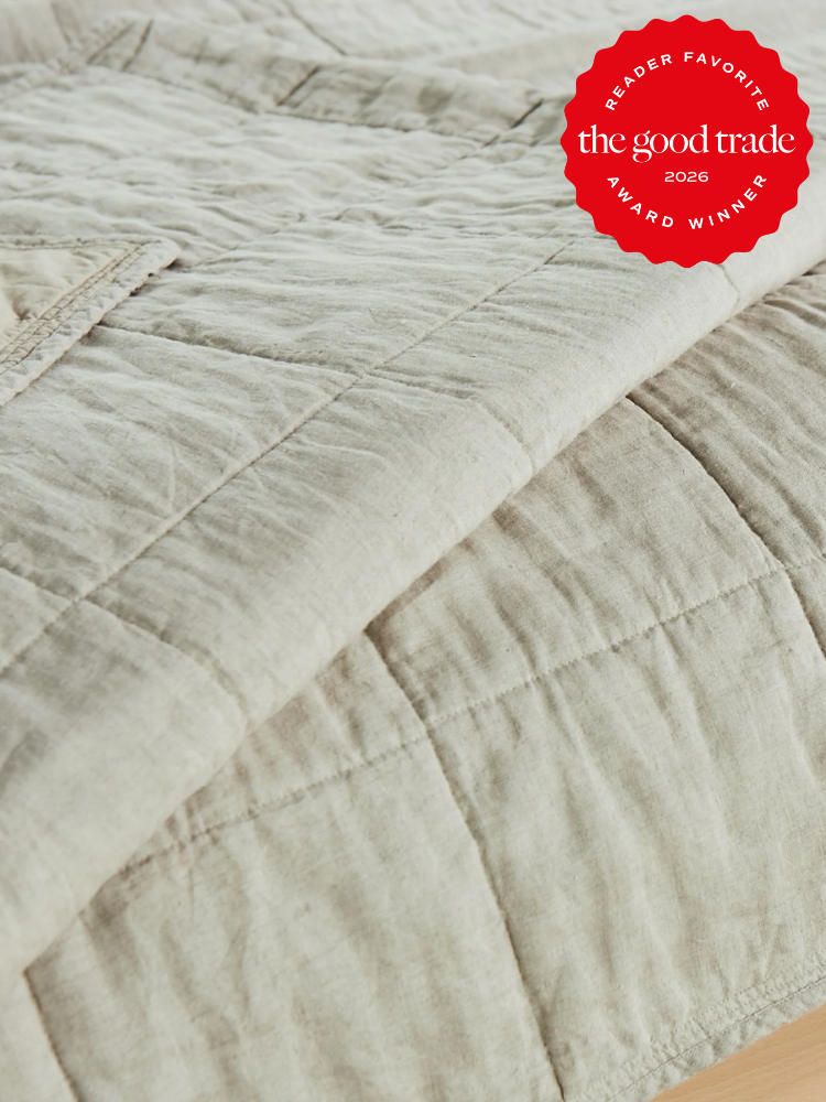 Close-up of a beige quilt with visible stitching on a bed, featuring a red “Reader Favorite The Good Trade Award Winner 2026” badge in the corner.