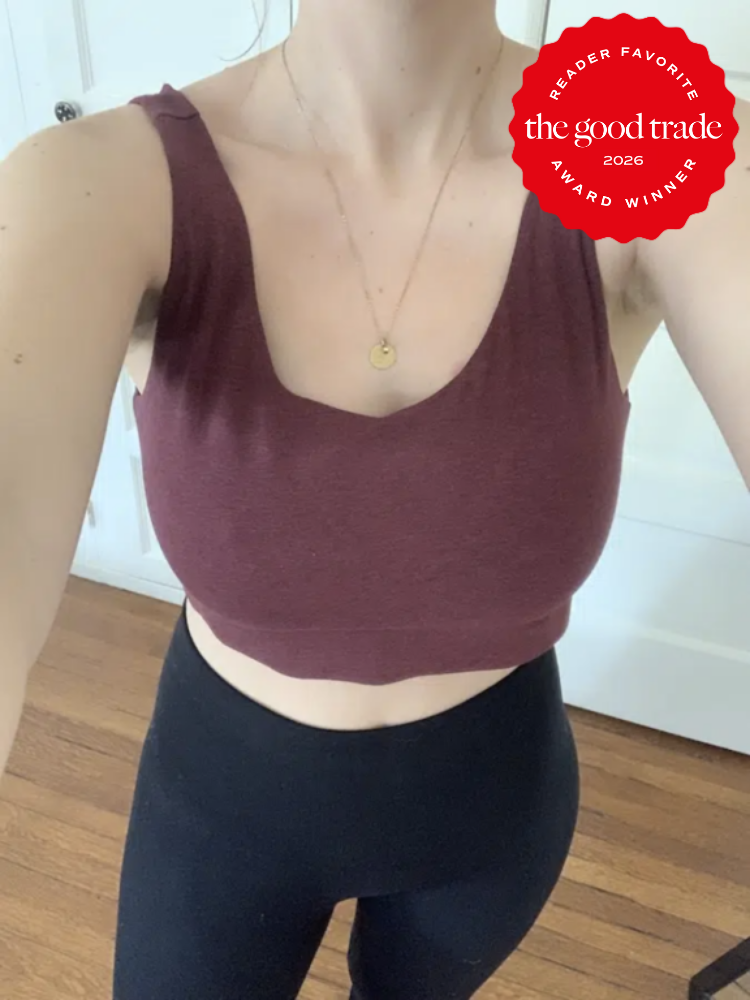 Person wearing a sleeveless maroon crop top and black leggings standing on a wooden floor. A red badge in the corner reads "the good trade award winner 2026 reader favorite.