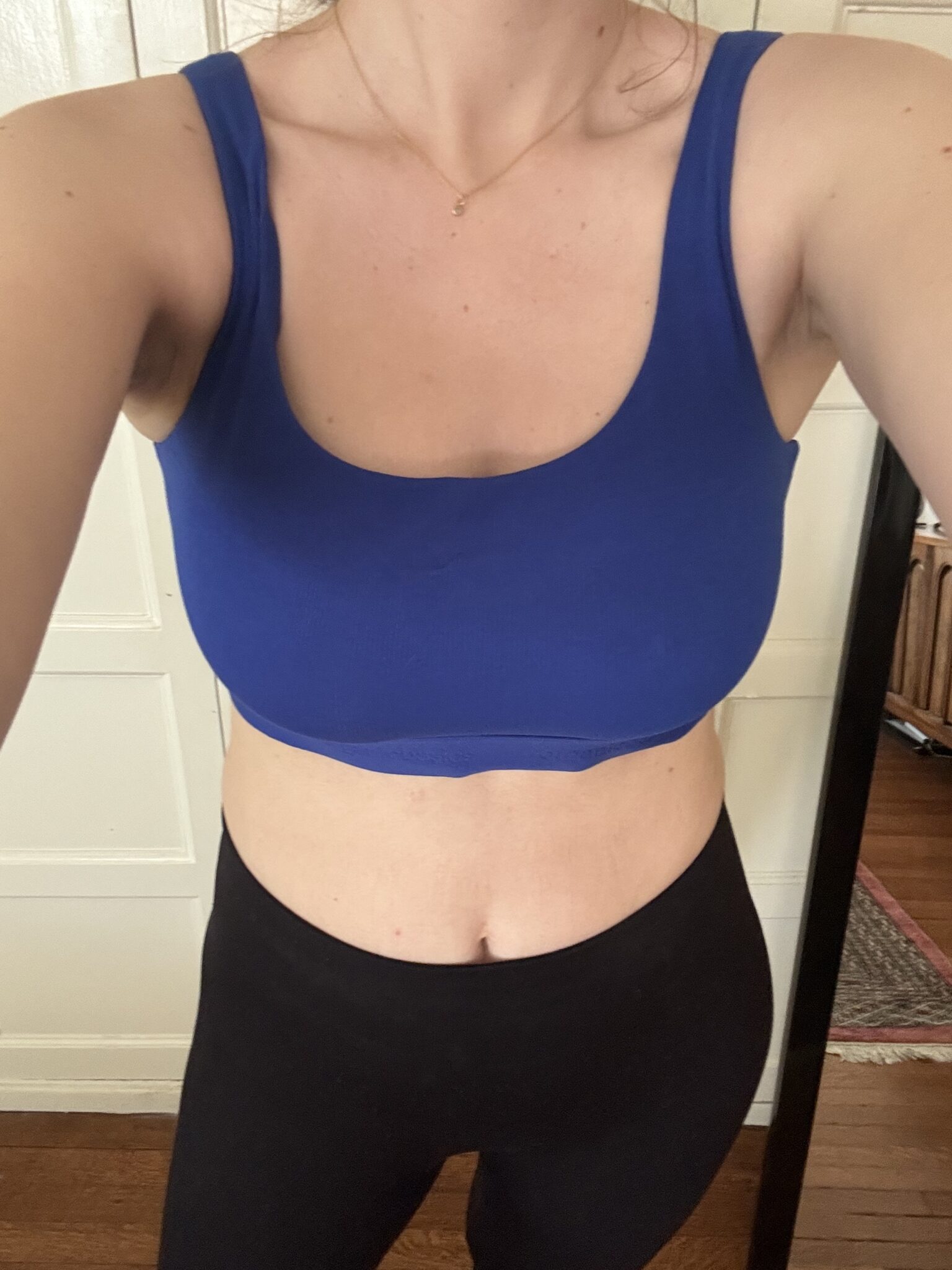 A person wearing a blue sports bra and black leggings stands indoors, photographed from the chest down.