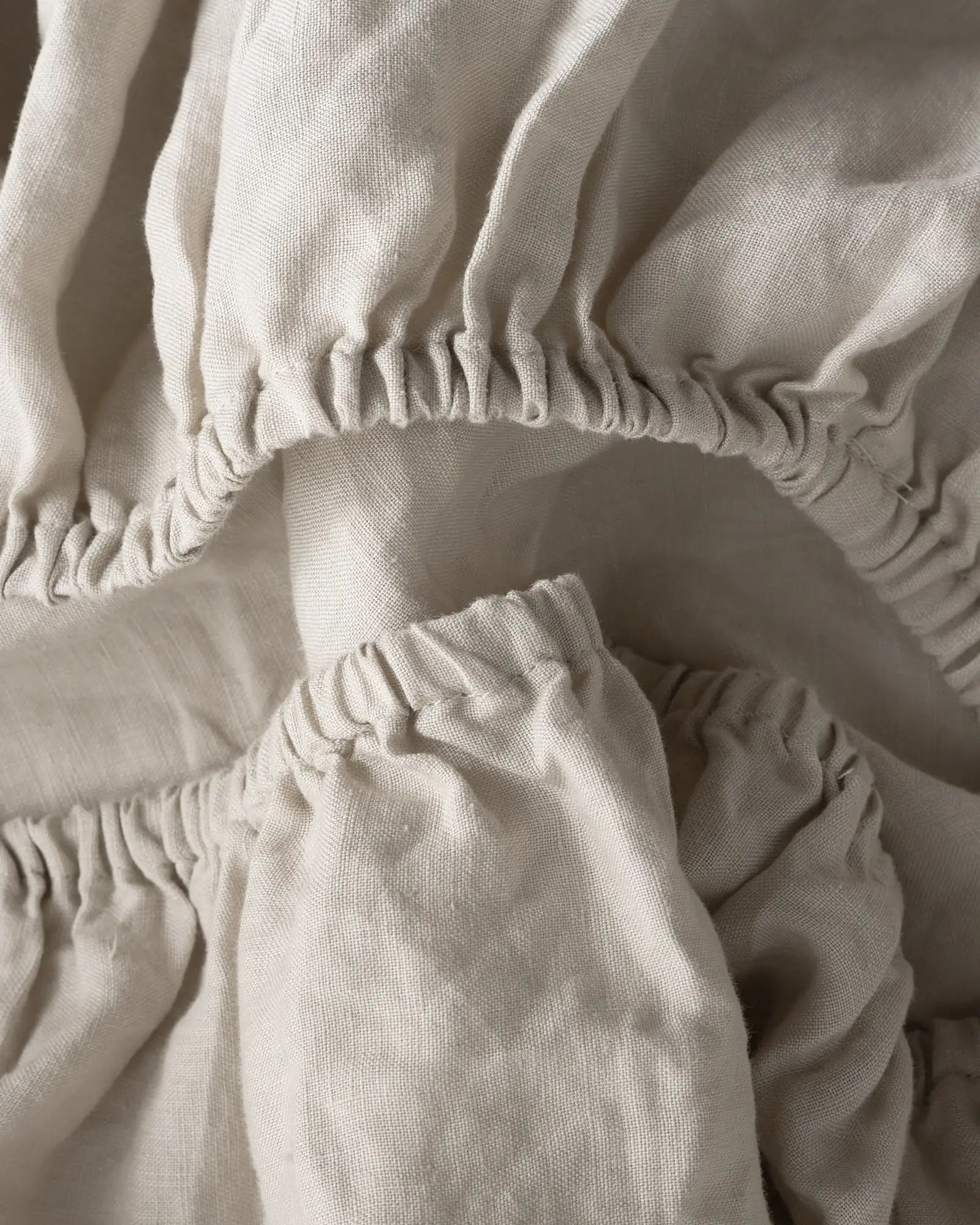 Close-up of beige fabric featuring gathered, elasticized seams arranged in overlapping layers.