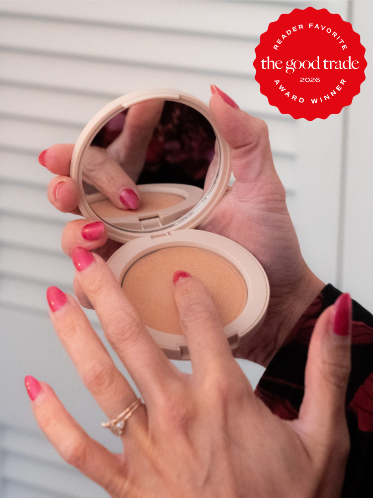 A person with pink nail polish uses a powder compact with a mirror. A red badge in the corner reads, "The Good Trade Award Winner 2026 Reader Favorite.