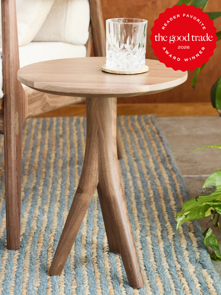 A round wooden side table with three legs holds a glass of water on a coaster; a red award badge is displayed in the upper right corner.