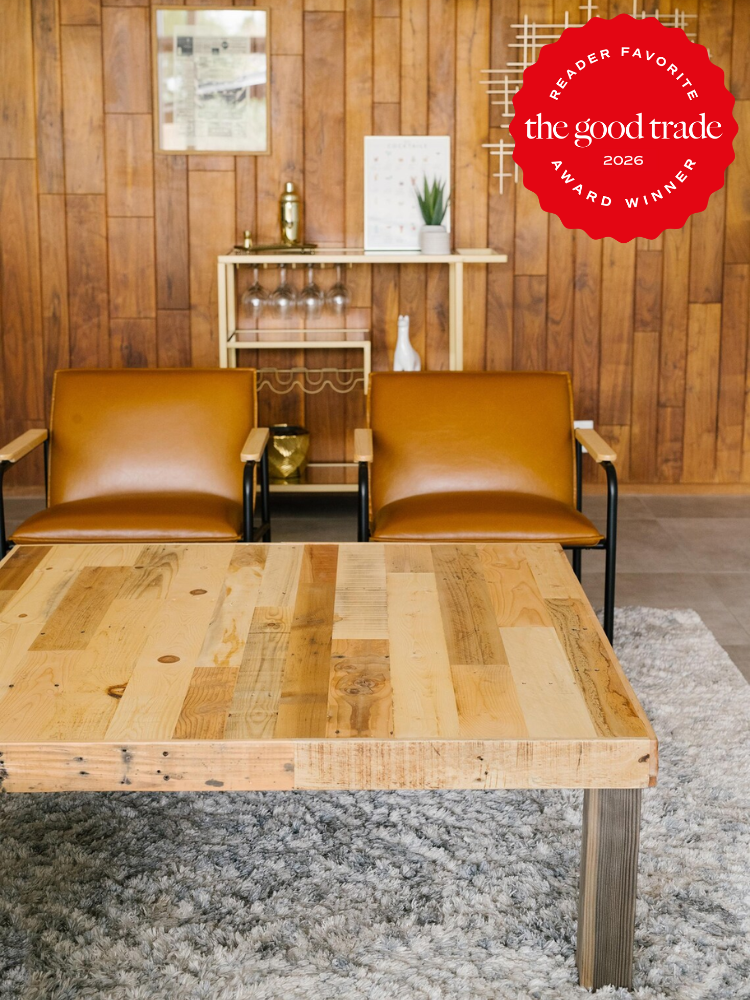 Two brown chairs and a wooden coffee table on a gray rug, with a wooden wall and shelving in the background. A red “The Good Trade 2026 Award Winner” badge is in the top right corner.
