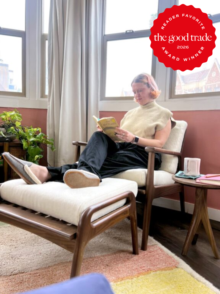 A person sits in a modern wooden chair by a window, reading a book. A red badge in the corner reads “The Good Trade Award Winner 2026.”.