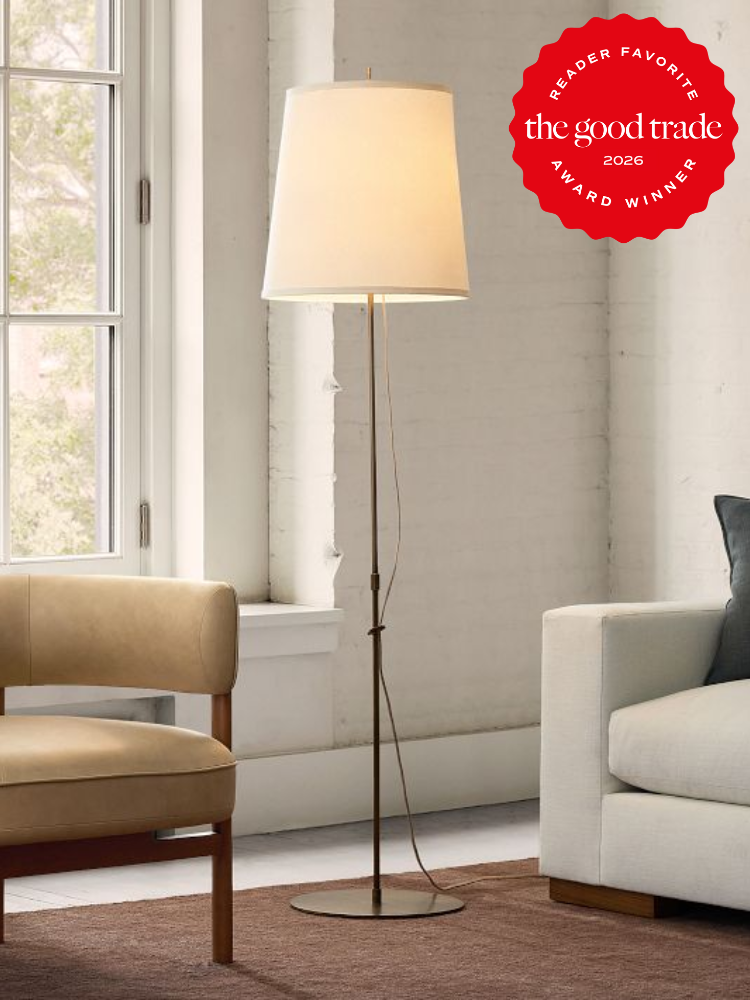 A tall floor lamp with a white shade stands between two neutral-colored chairs in a bright room with white brick walls and large windows. A red award badge appears in the top right corner.