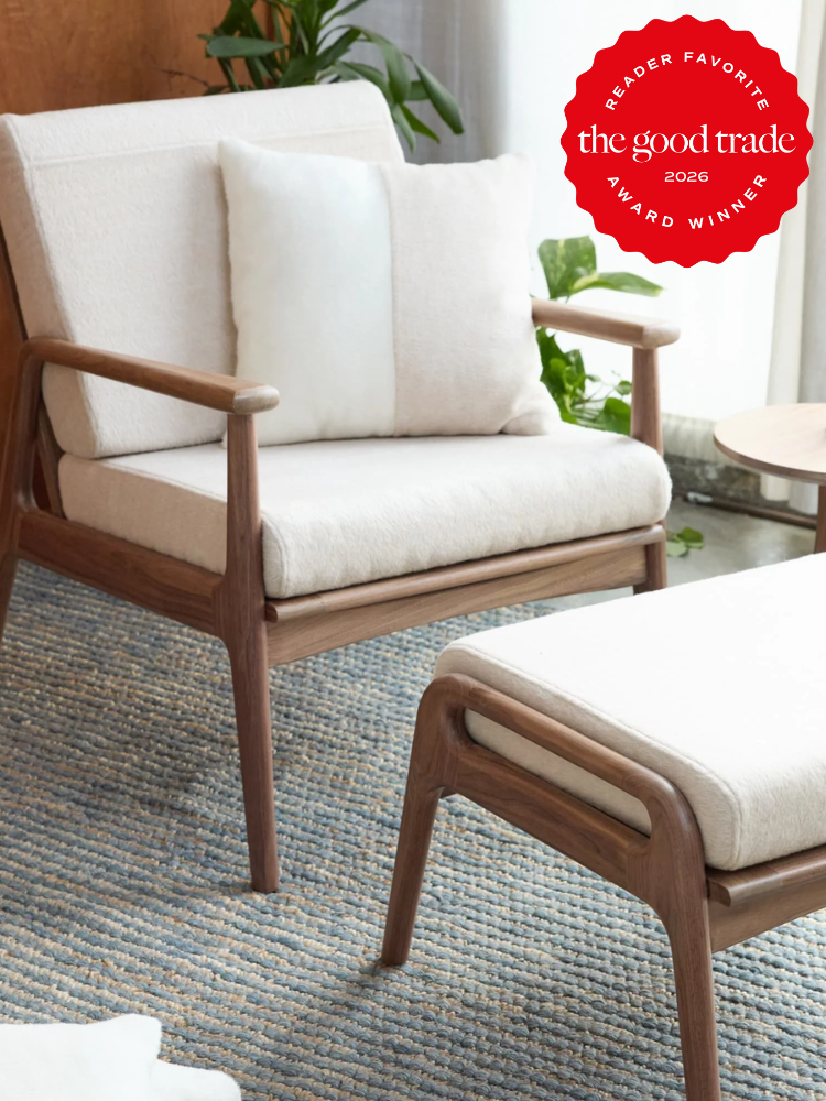 A wooden armchair with cream cushions and a matching ottoman on a blue woven rug; a "The Good Trade 2026 Award Winner" badge is in the top right corner.
