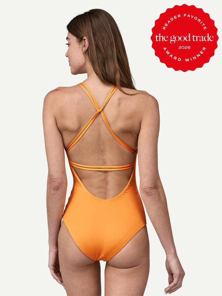A woman models an orange one-piece swimsuit with crisscross straps on the back. A red badge reads "The Good Trade Reader Favorite Award Winner 2026.