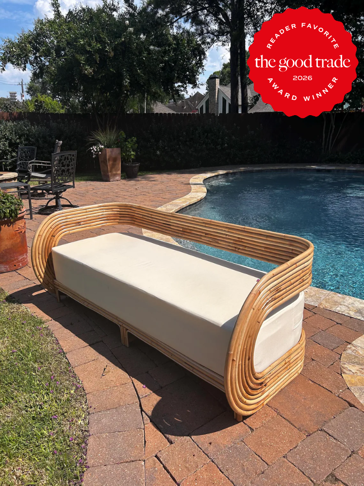 A bamboo-framed outdoor sofa with white cushions is placed on a brick patio beside a backyard pool. A red award badge in the corner reads "The Good Trade Reader Favorite 2026 Award Winner.