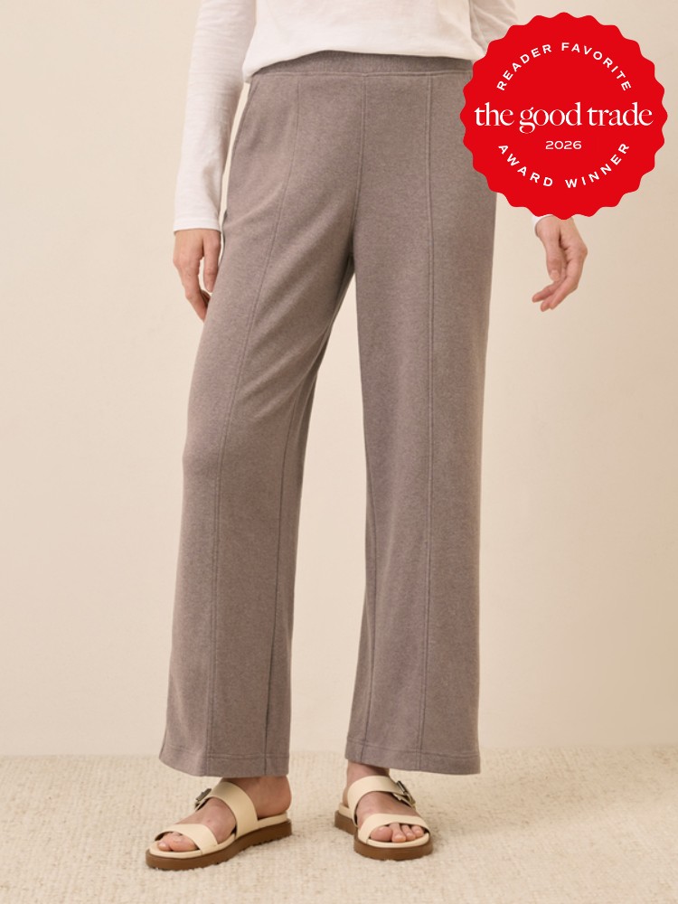 Person wearing grey wide-leg knit pants, a white long-sleeve top, and beige sandals. A red "The Good Trade Award Winner 2026" badge is in the top right corner.