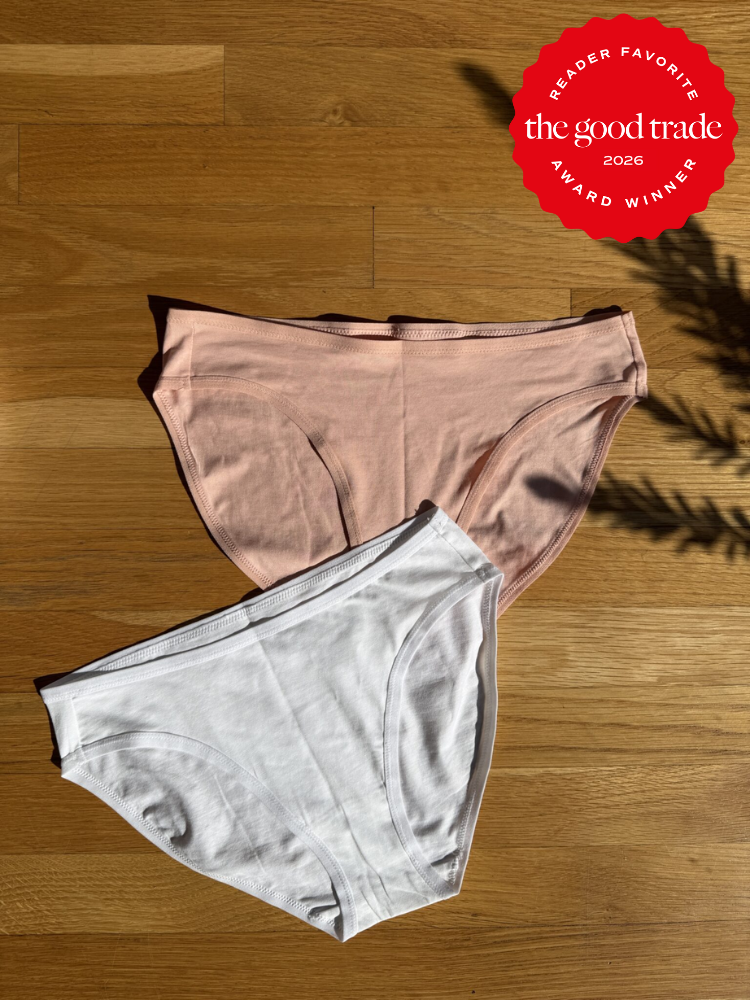 Two pairs of cotton underwear, one pink and one white, are laid flat on a wooden surface. A red award badge appears in the top right corner.