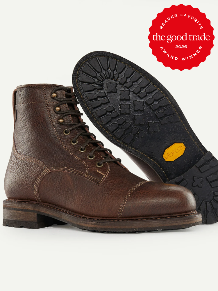 A pair of brown leather lace-up mens boots, one upright and one showing the sole, with a red "The Good Trade Award Winner 2026" badge in the corner.