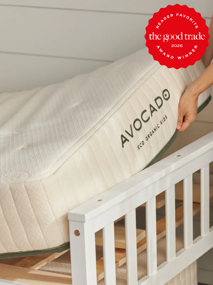 A person places an Avocado Eco Organic Kids mattress in a white crib; the image features a “Reader Favorite 2026 Award Winner” badge from The Good Trade.