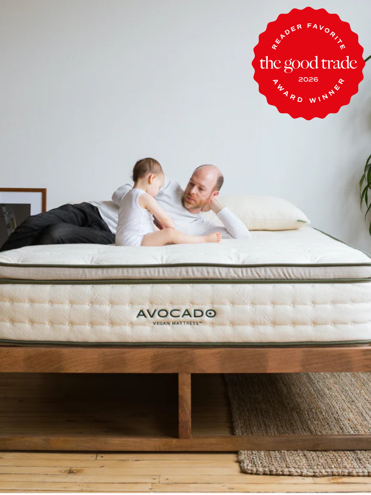 An adult and a child sit on an Avocado vegan mattress in a minimal bedroom. A red badge in the corner reads "The Good Trade Reader Favorite Award Winner 2026.