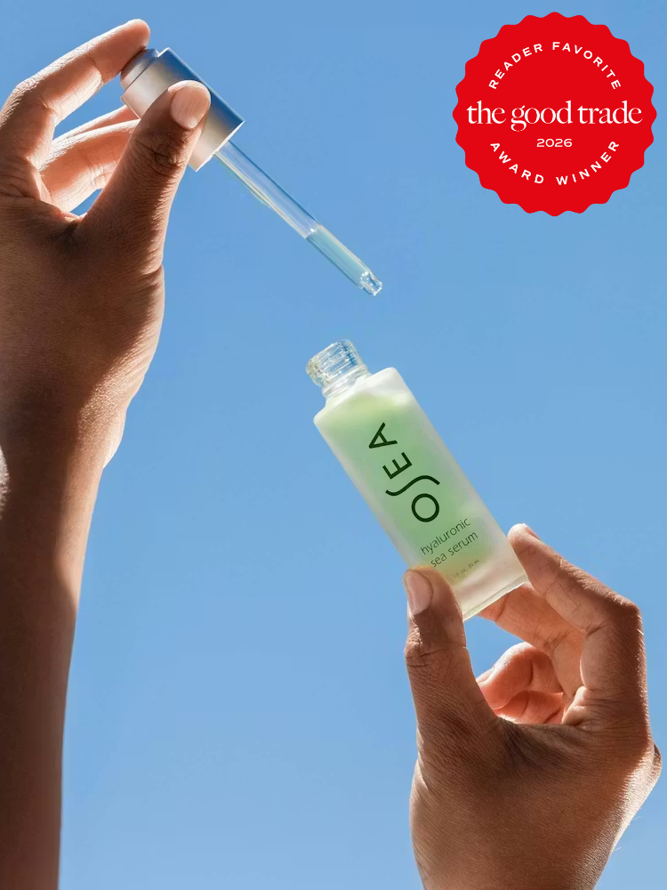 A person holds a dropper and an open bottle of OSEA hyaluronic sea serum against a clear blue sky. A red "The Good Trade 2026 Award Winner" badge is in the top right corner.