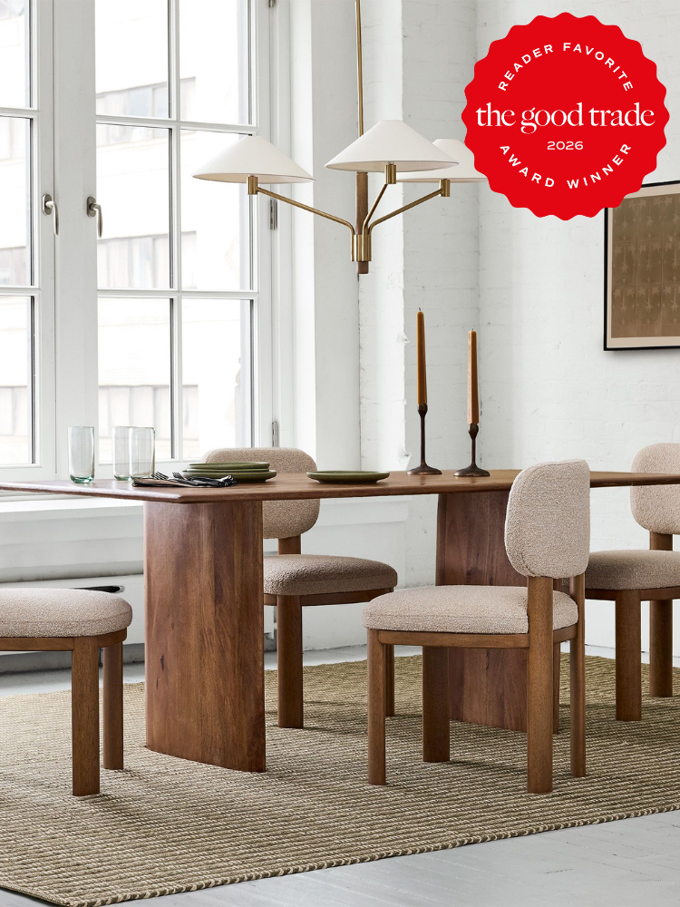 Modern dining room with a wooden table, four upholstered chairs, two candles, glassware, and a pendant light, set on a woven rug by large windows; award badge in upper right corner.
