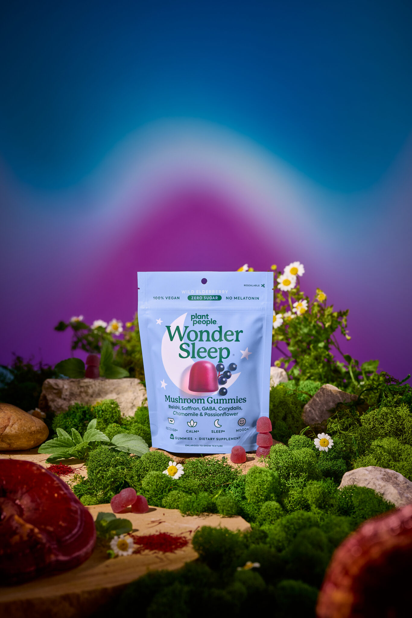 A package of WonderSleep mushroom gummies stands on moss surrounded by flowers and greenery, with a few gummies placed in front, against a colorful gradient background.