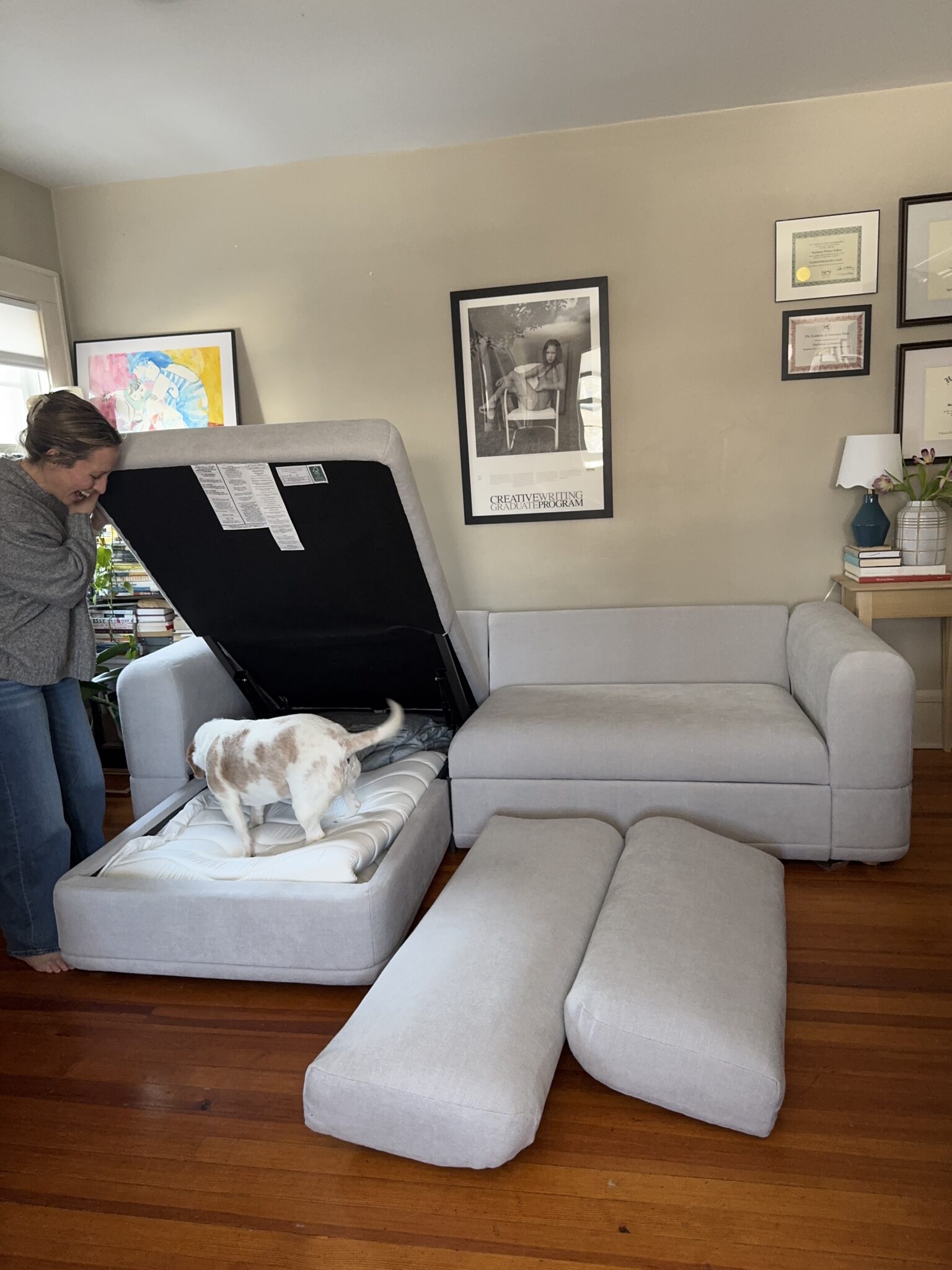 A woman and a dog stand by a light gray sectional sofa with the storage compartment open and cushions removed in a living room.