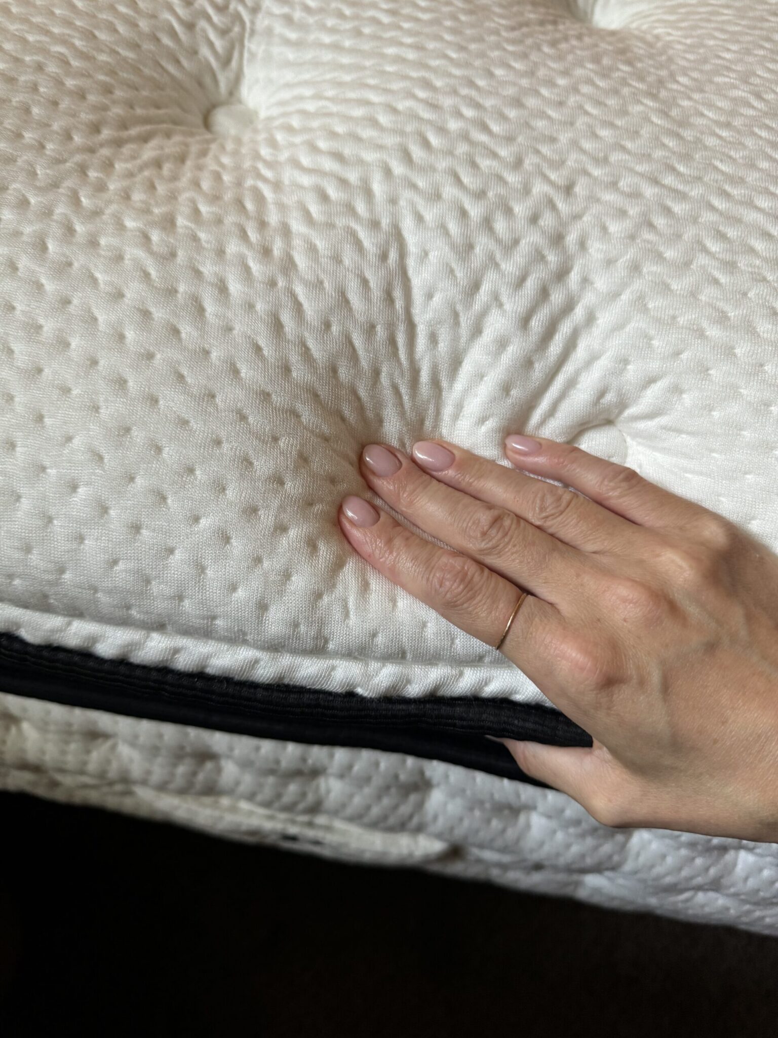 A hand presses down on a white, textured latex mattress surface with a black zipper along the edge.