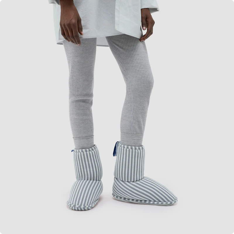 A person wearing gray ribbed leggings and cozy slippers stands against a plain light background.