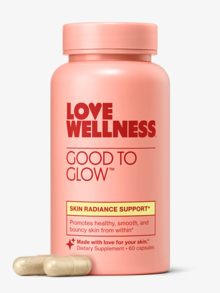 A pink bottle labeled "Love Wellness Good to Glow" skin radiance support supplement with two beige capsules beside it.