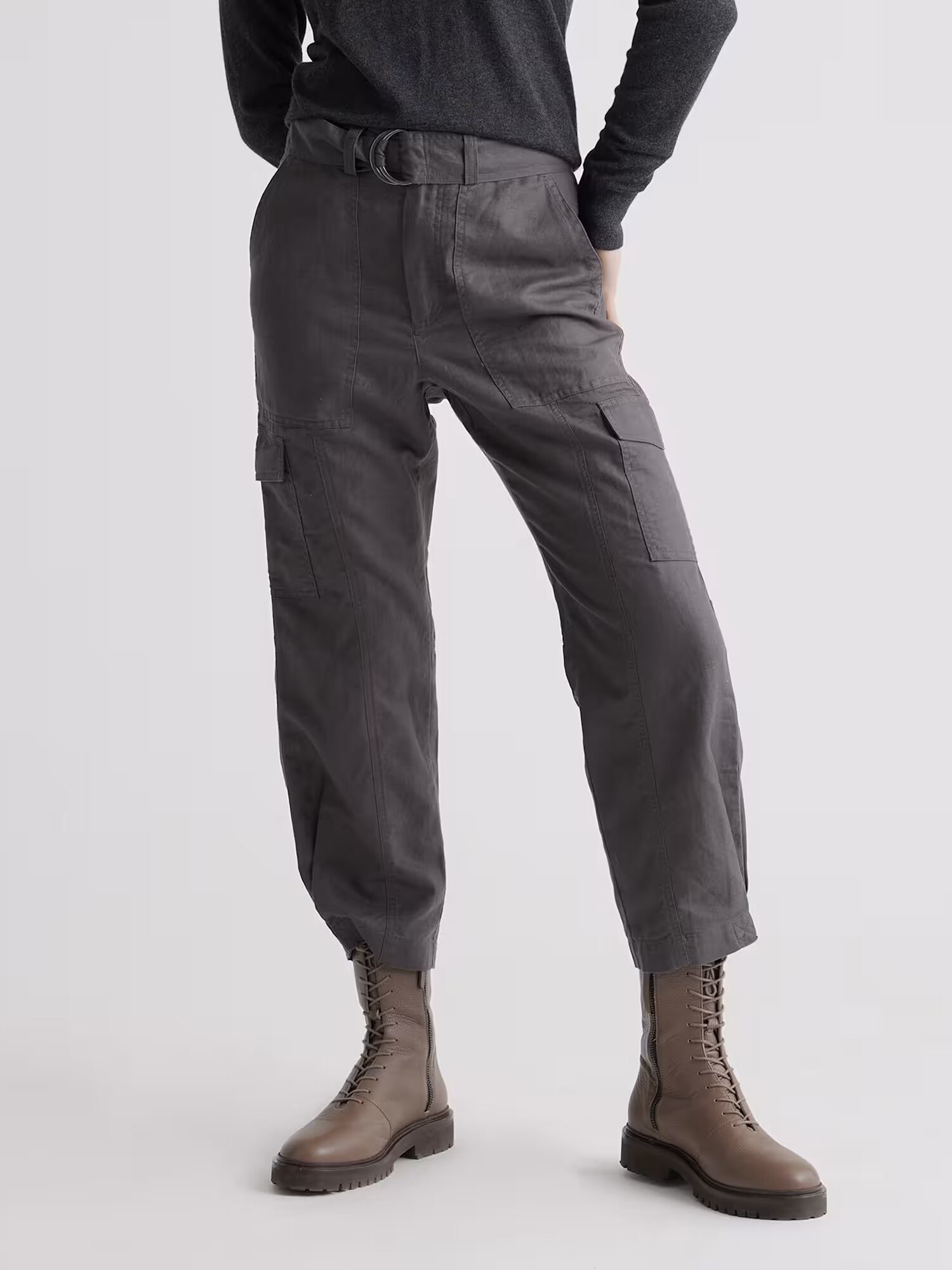 Person wearing charcoal gray cargo pants with a belt, dark top, and lace-up brown combat boots, standing against a plain light background.