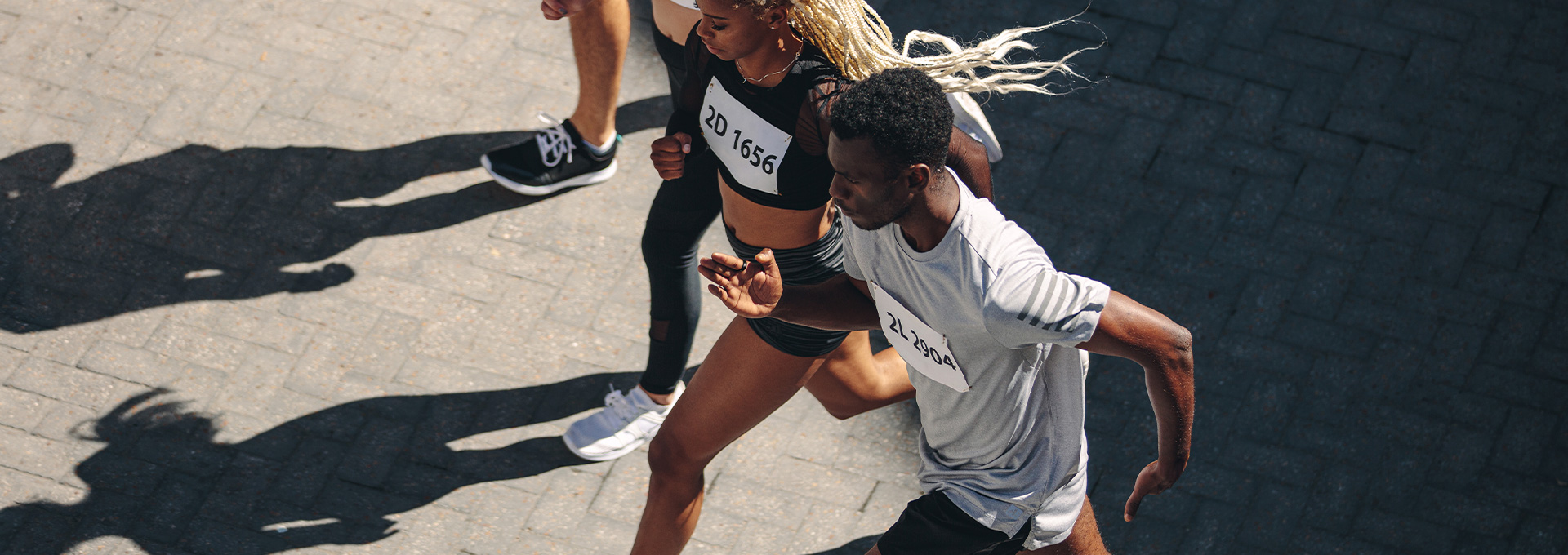 Overhead view of two athletes running side by side on a paved surface, wearing race bibs and athletic clothing.