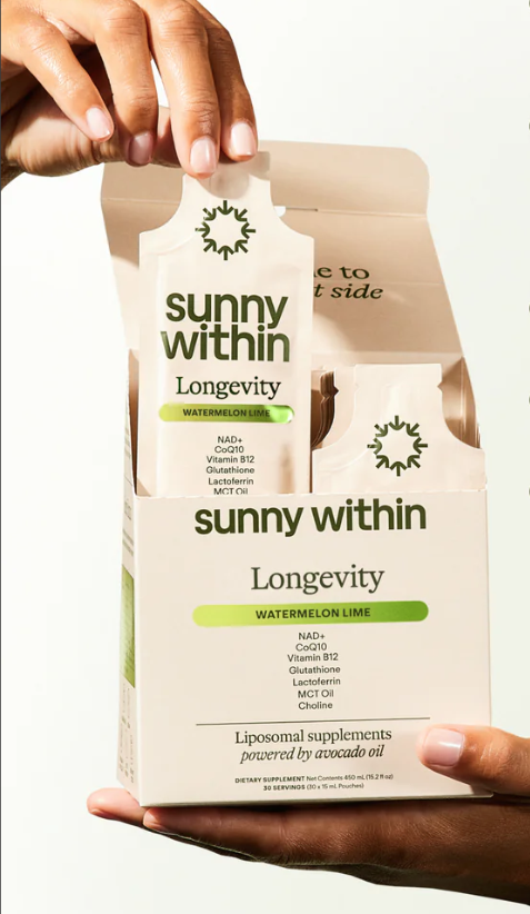 A person holds an open box of Sunny Within Longevity Watermelon Lime liposomal supplement packets, with one packet being lifted from the box.