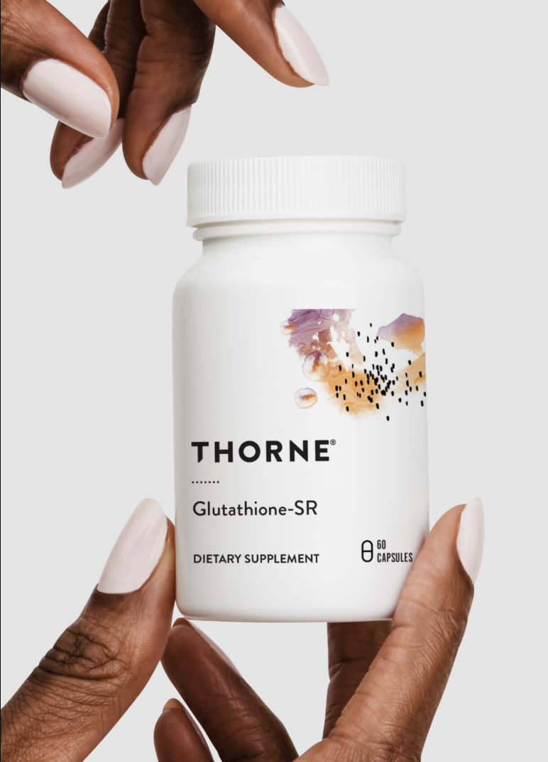 A person’s hands hold a white bottle labeled "Thorne Glutathione-SR Dietary Supplement, 60 capsules" against a plain background.