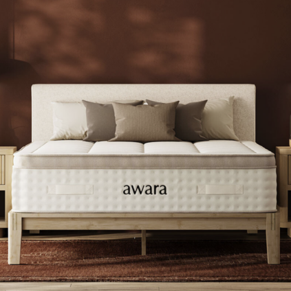 A bed with a beige headboard, neutral pillows, and an "awara" branded mattress sits between two wooden nightstands against a brown wall.
