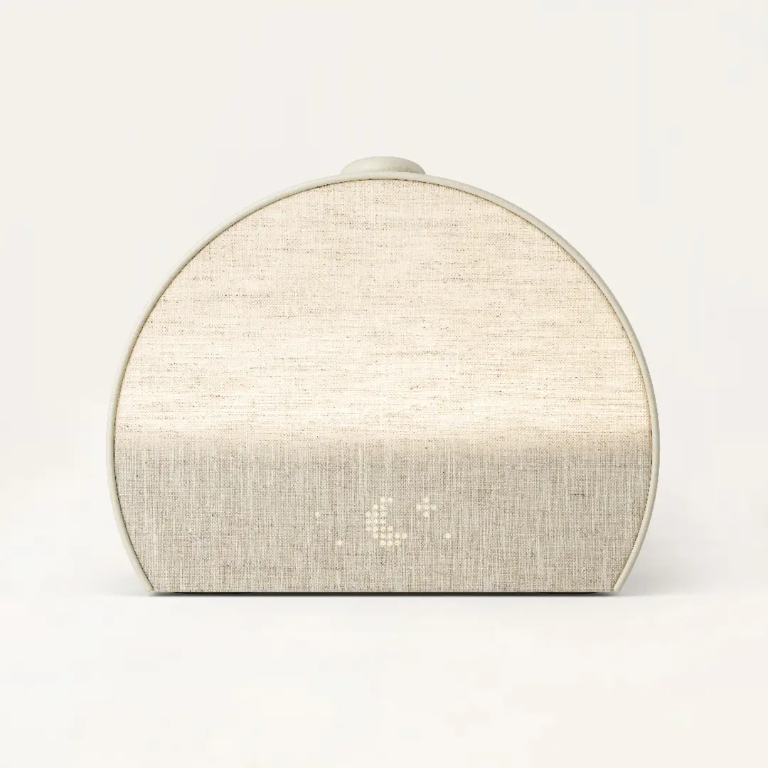 A beige, semicircular electronic device with a fabric front and subtle dot pattern, placed against a plain light background.