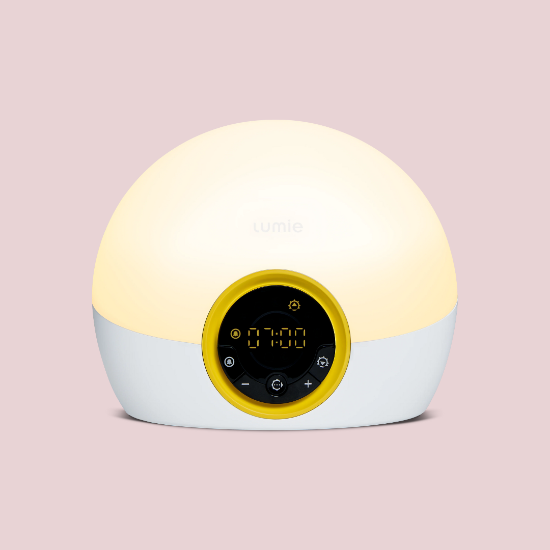 A dome-shaped sunrise alarm clock with a digital display and control buttons on a light pink background.